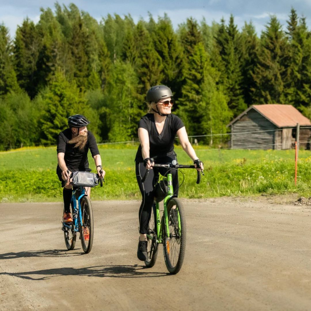 Kaksi henkilöä melovat vihreällä kanootilla järvellä, punaiset pelastusliivit ja aurinkoinen taivas.